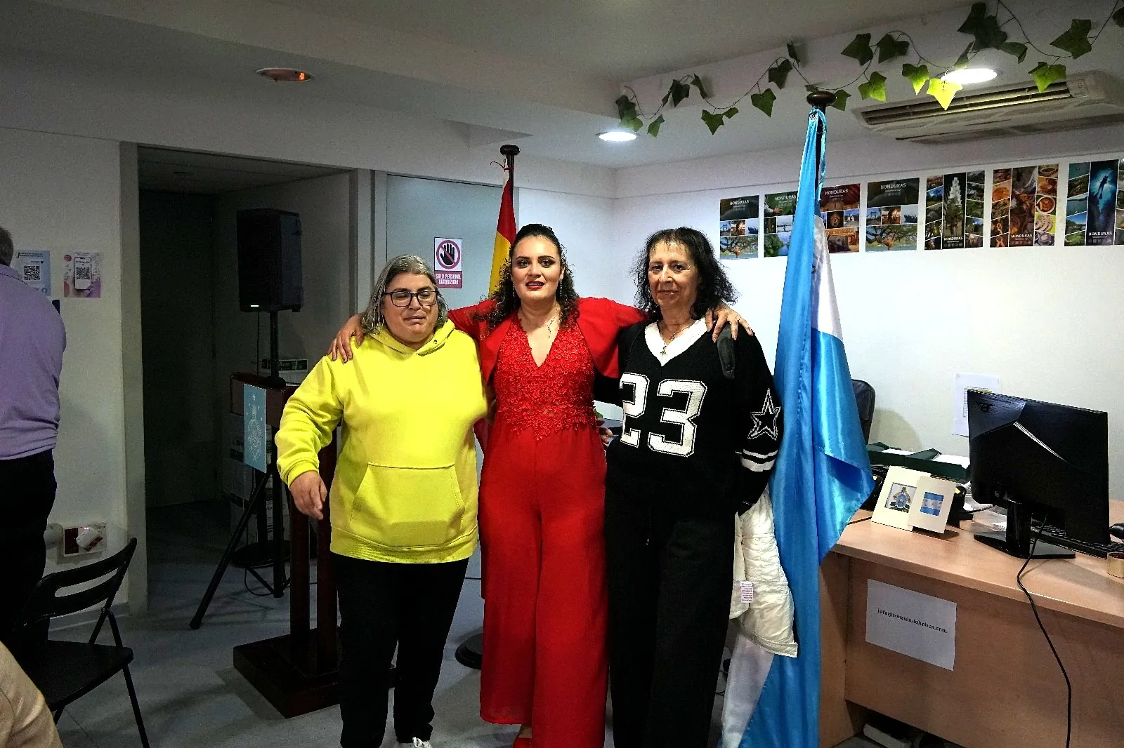 Yadi Villanueva abrazada a dos asistentes junto a la bandera de Honduras en el Consulado