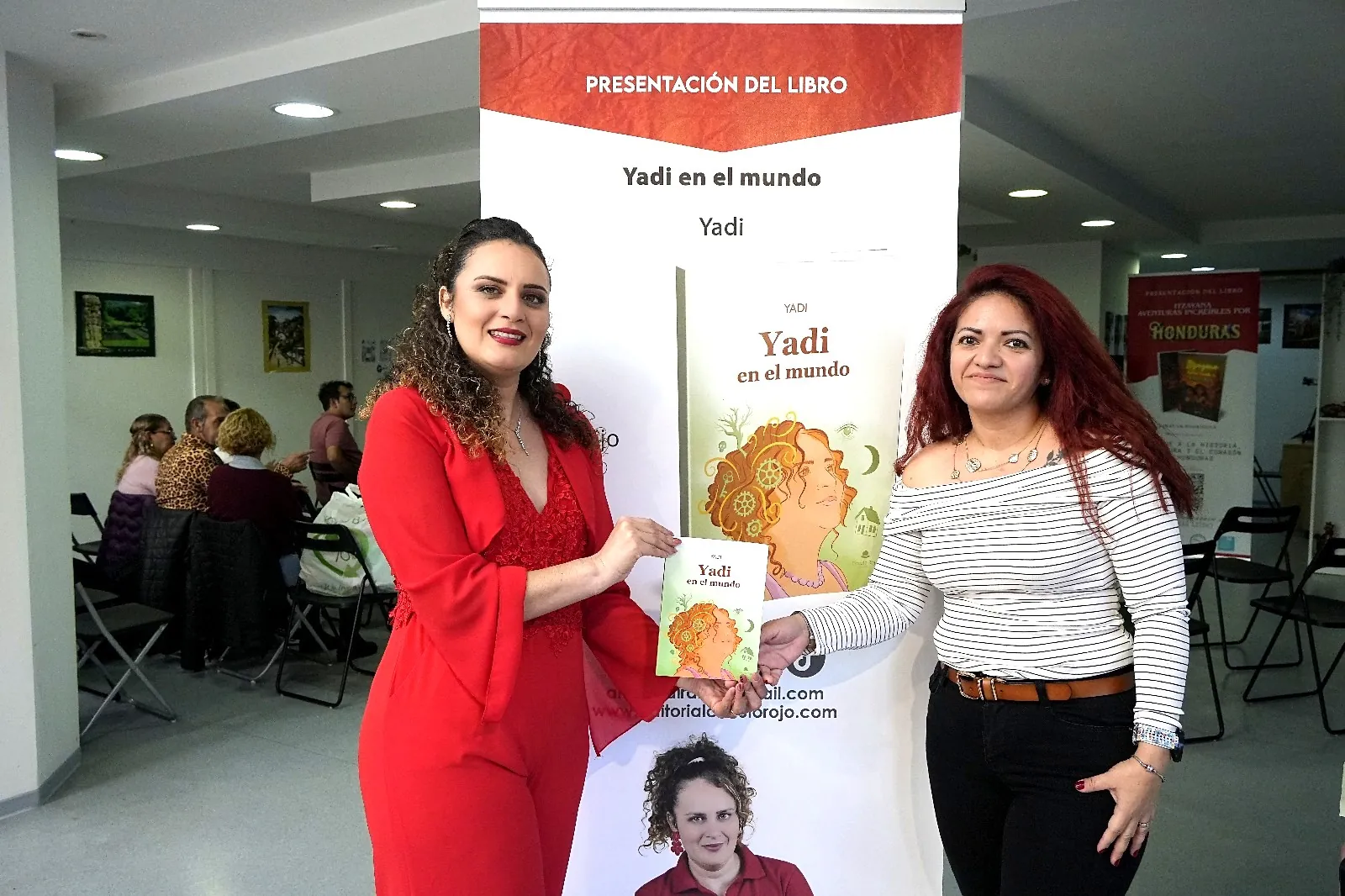 Yadi Villanueva compartiendo su libro con una lectora ante el cartel de la presentación