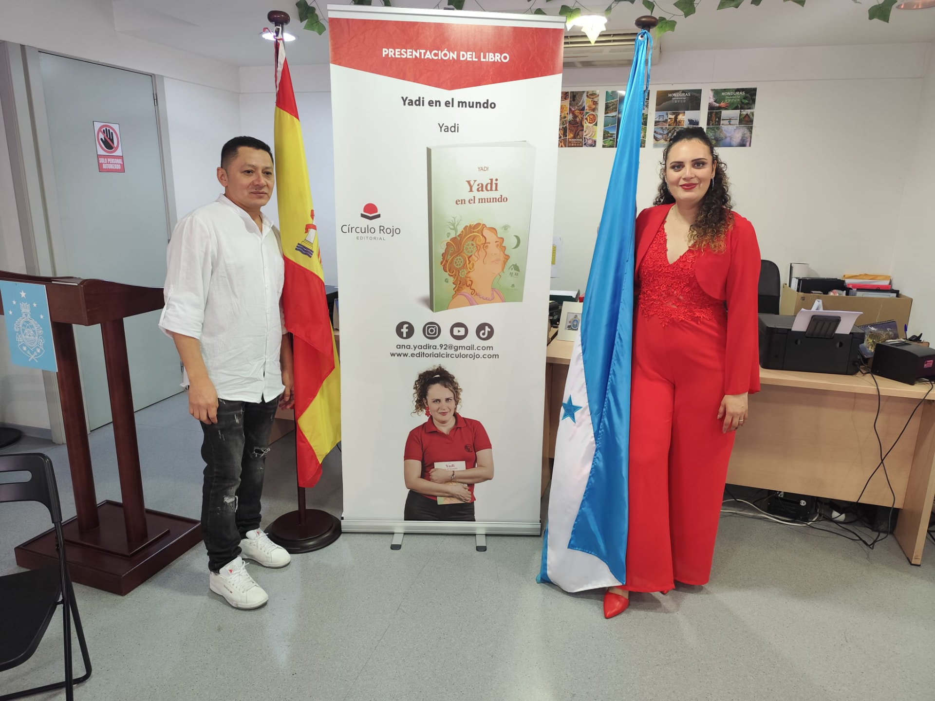 Yadi Villanueva e invitado junto al cartel de Yadi en el mundo en el Consulado General de Honduras