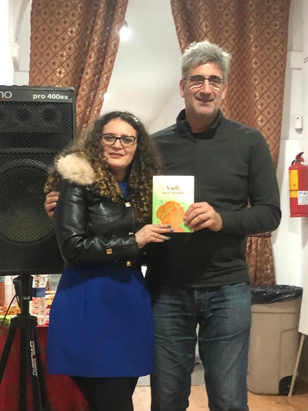 Yadi Villanueva sosteniendo su libro junto a un asistente en la presentación en FEDELATINA