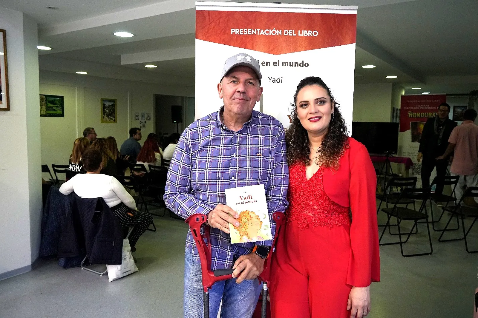 Un asistente sostiene el libro Yadi en el mundo junto a la autora en el Consulado de Honduras