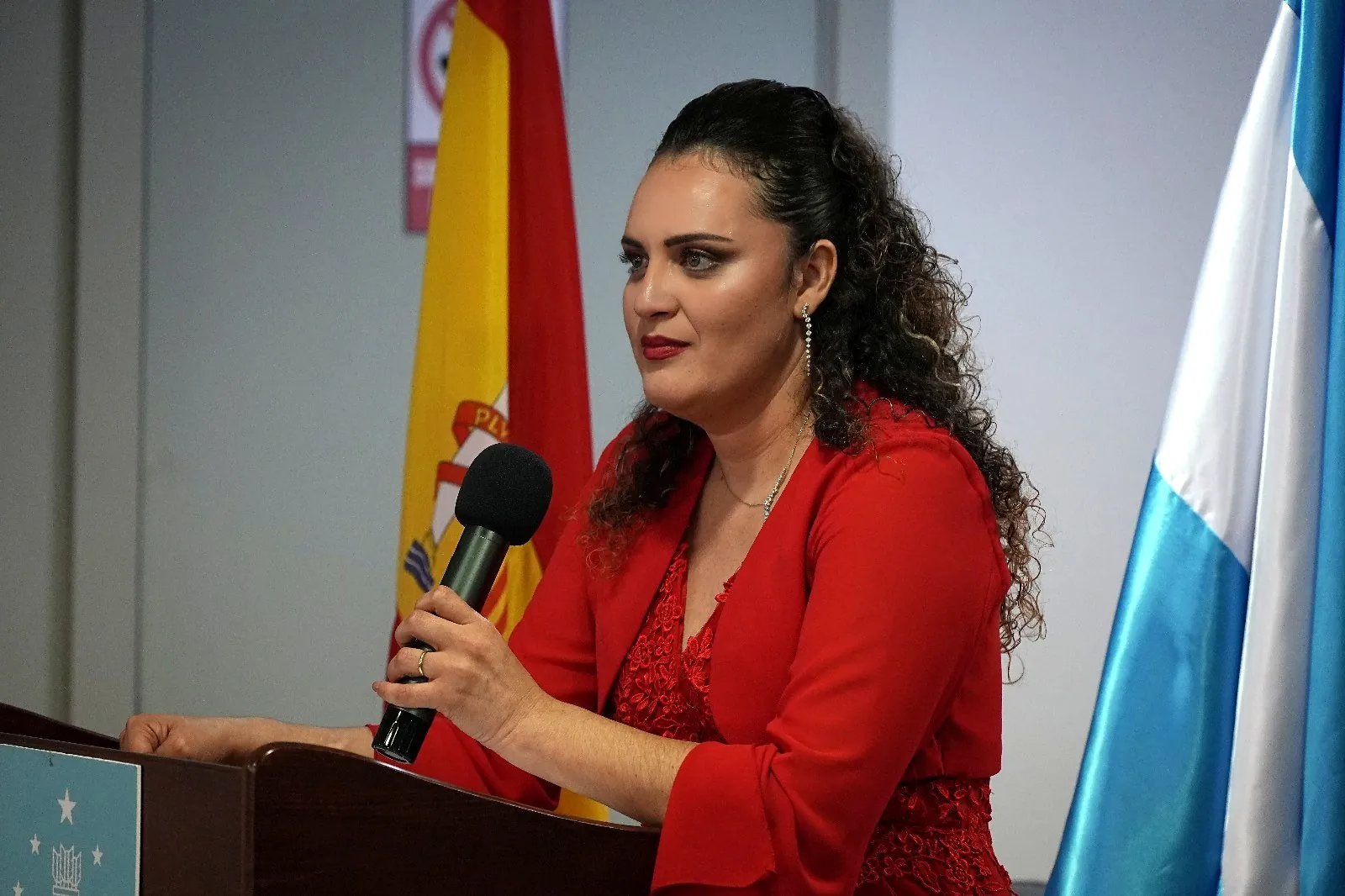 Yadi Villanueva hablando con micrófono en el atril durante la presentación en el Consulado de Honduras