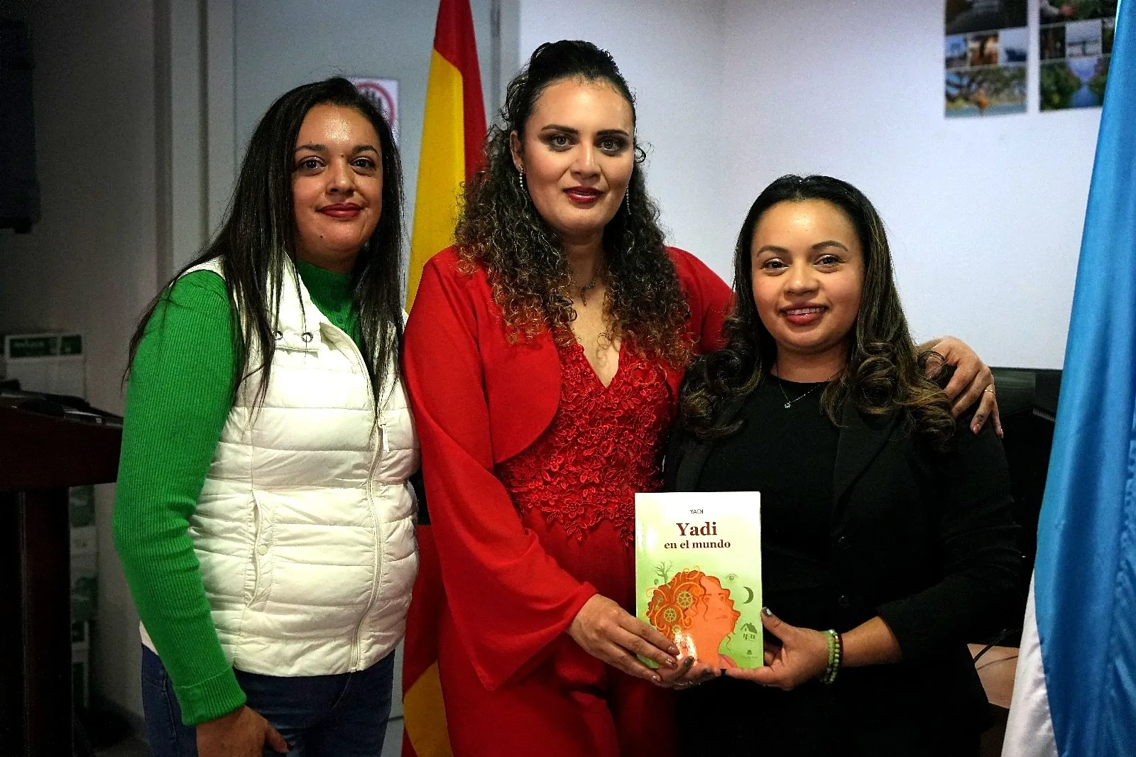 Yadi Villanueva con dos asistentes sosteniendo su libro ante las banderas de España y Honduras